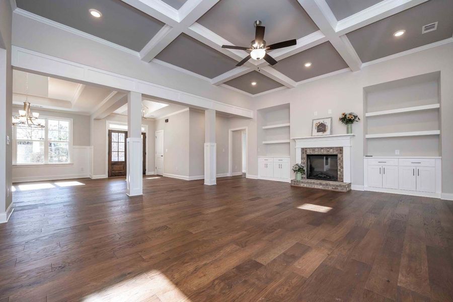 Spacious living room with hardwood floors, gray coffered ceiling, fireplace, built-in shelves, and windows.