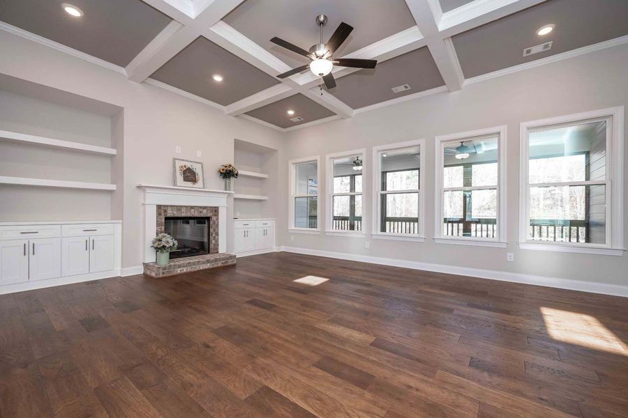 Spacious living room with hardwood floors, fireplace, built-in shelves, and large windows.