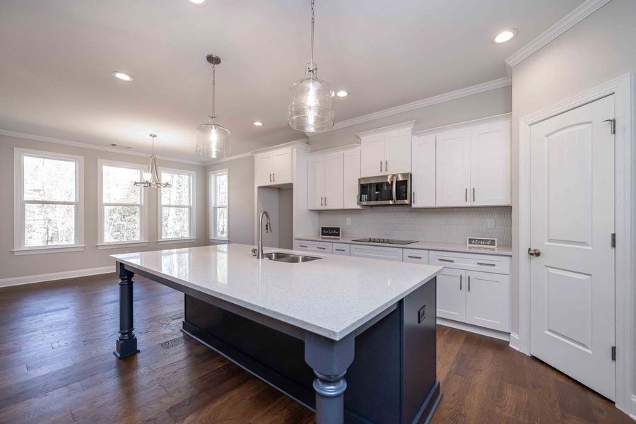Spacious kitchen with white cabinets, island, hardwood floors, and natural light from windows.