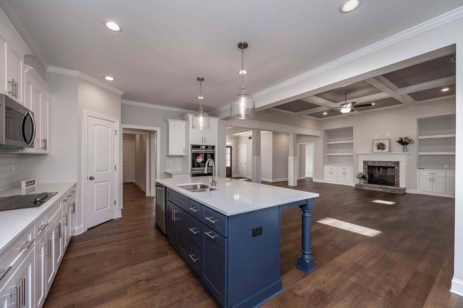 Modern kitchen with blue island and white cabinets, open to living area with fireplace.