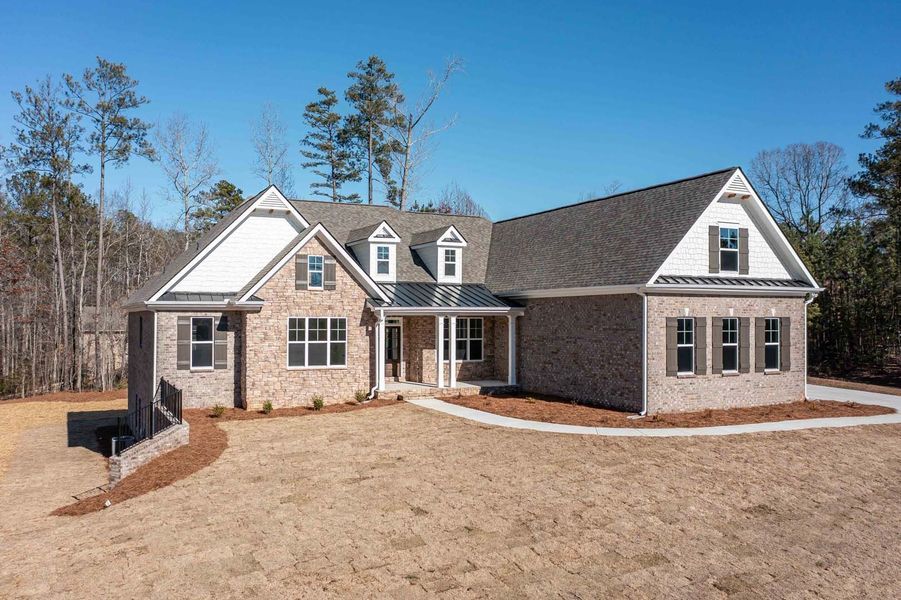Brick house with brown shutters, a covered porch, and dormer windows on a sunny day.