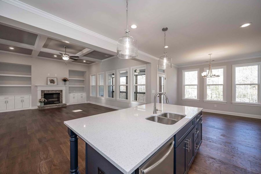 Spacious open-concept kitchen and living room. Blue island, white countertop, dark wood floors, white walls, fireplace.