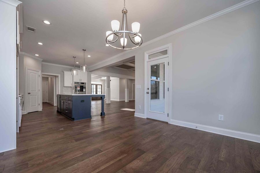 Spacious kitchen and dining area with dark hardwood floors and gray walls, connected to a hallway.