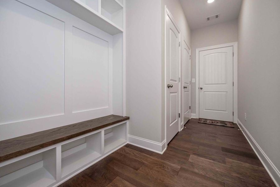 Entryway with white built-in bench, shelves, and wood floor. White doors and walls lead to another door.