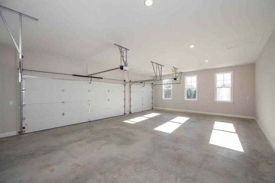 Empty two-car garage with white doors and concrete floor, lit by sunlight streaming through windows.