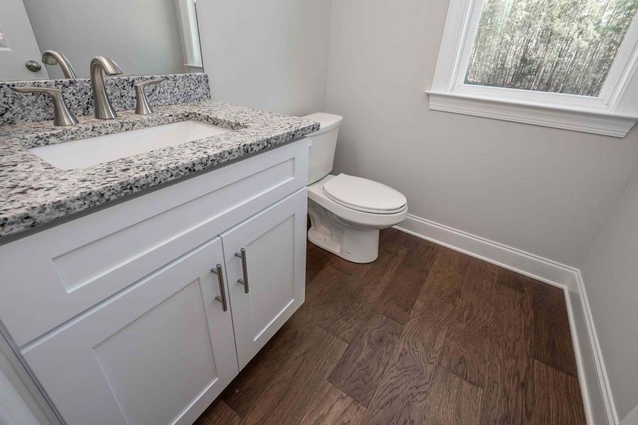 A small, white bathroom with a vanity, toilet, and dark wood-look flooring.
