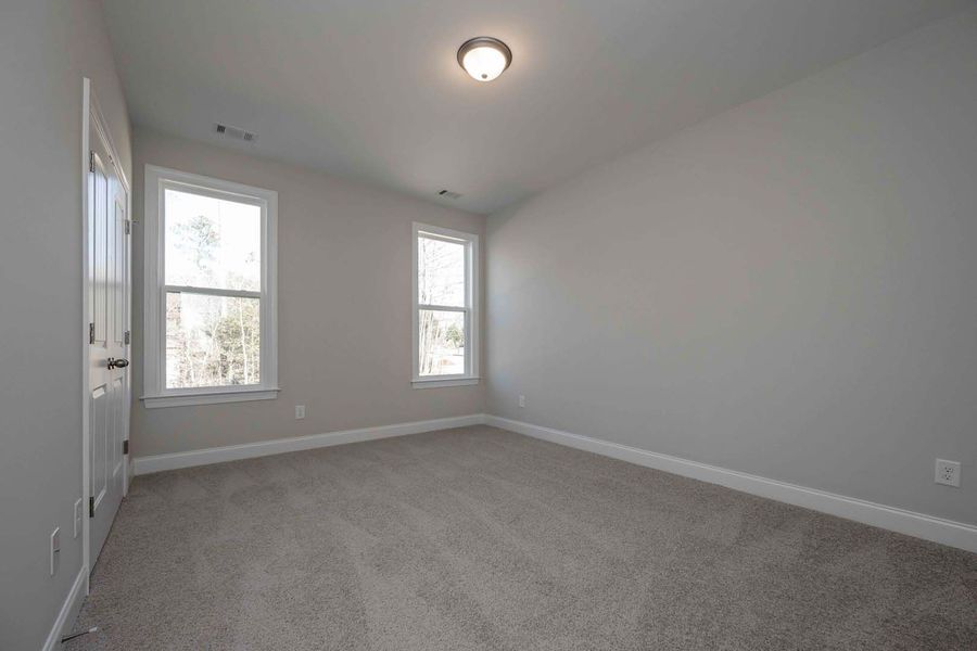 Empty bedroom with gray walls and carpet; two windows and a ceiling light.