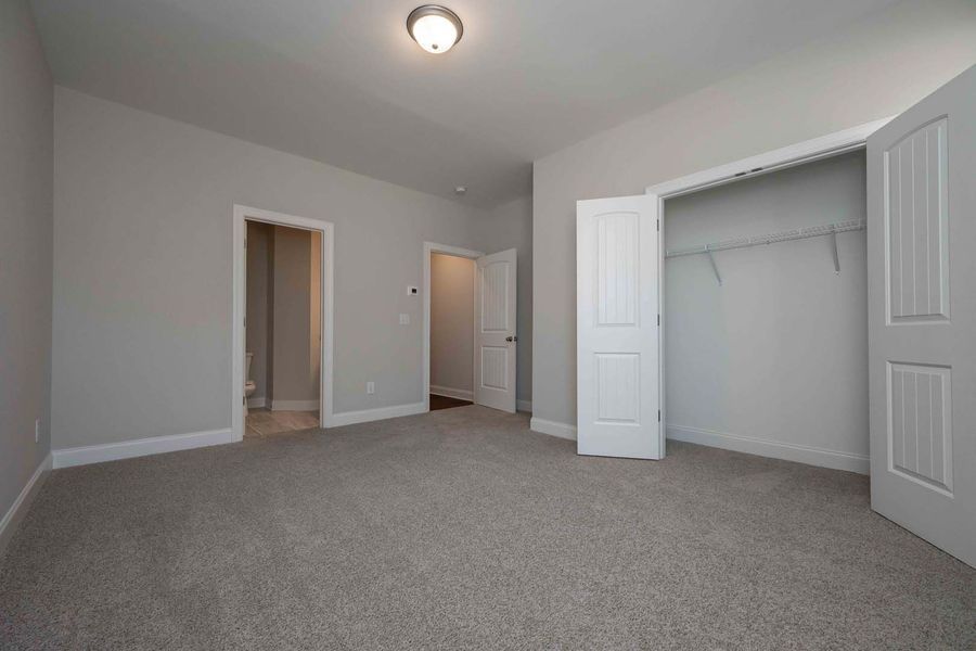Empty bedroom with gray carpet, white closet doors, and a door leading to a bathroom.