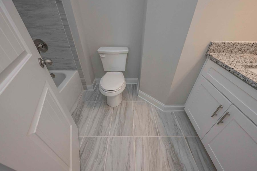 Bathroom with toilet, tub, white cabinets, and gray tile flooring.