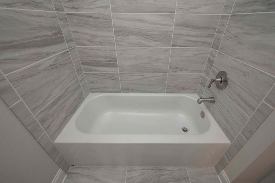 White bathtub with silver faucet, surrounded by gray marbled tiles in a bathroom setting.