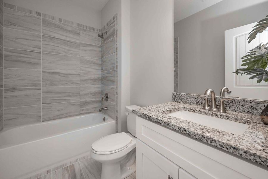 Bathroom with white vanity, granite countertop, toilet, bathtub, and marble tile walls.