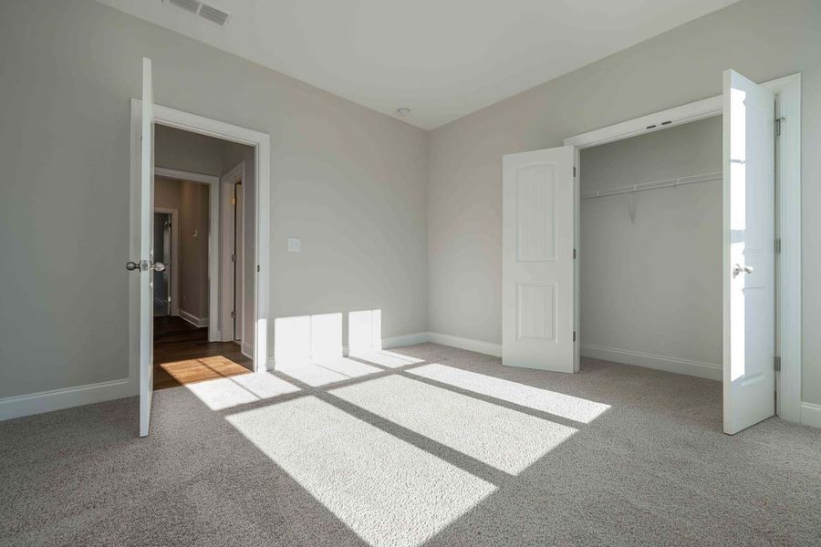 Empty bedroom with gray walls, carpet, and white doors; sunlight across floor.