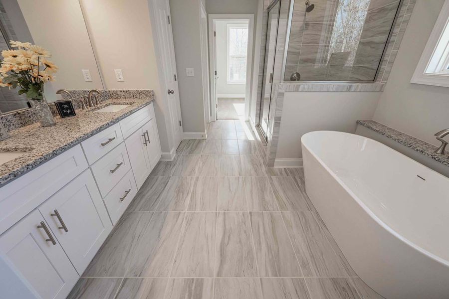 Spacious modern bathroom with white cabinetry, gray granite countertops, freestanding tub, and wood-look tile floors.