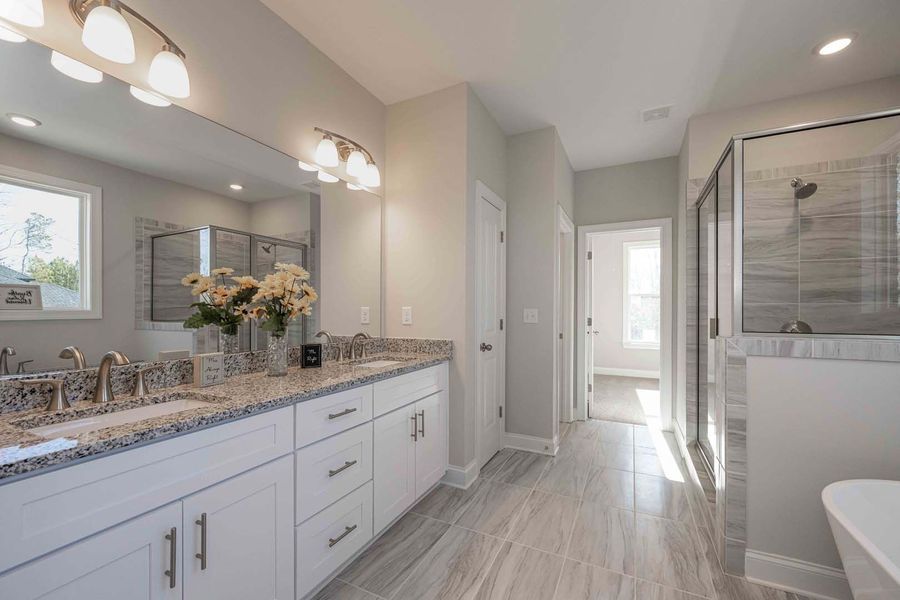 Modern bathroom with white cabinetry, granite countertops, large mirror, and glass shower.
