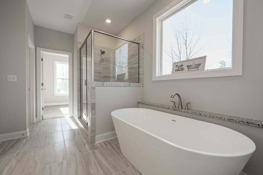 Modern bathroom with white freestanding tub, glass shower, and large window.