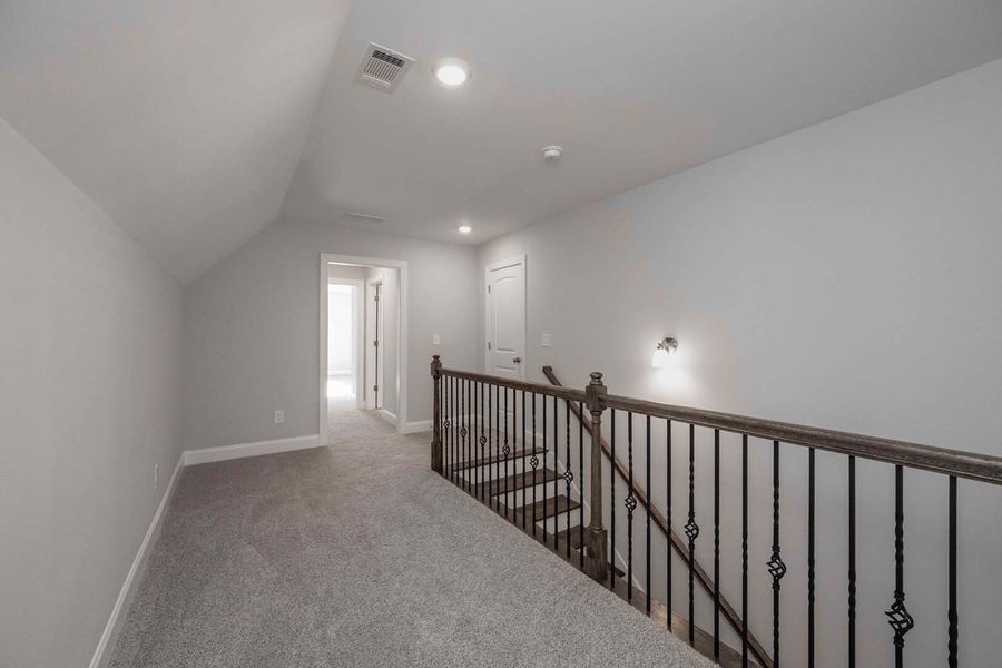 Hallway with stairs and carpet. Gray walls and railing.