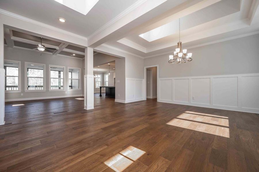 Spacious interior with hardwood floors, white walls, and a chandelier. Sunlight streams through windows.