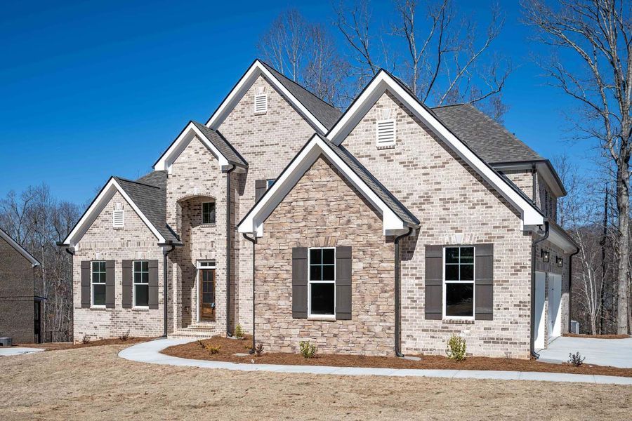 Two-story brick house with multiple gables, dark shutters, and gray roof against a clear blue sky.
