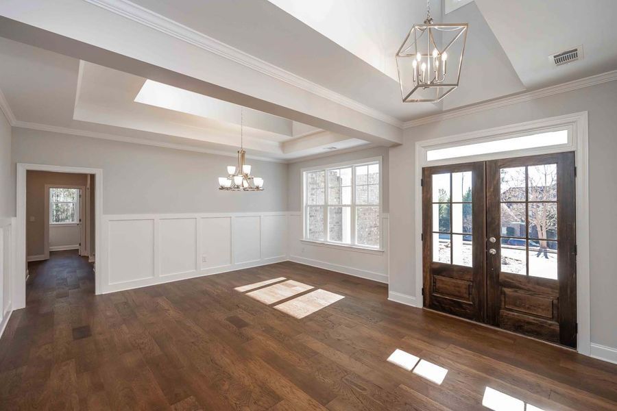 Empty dining room with hardwood floors, light gray walls, and dark wood double doors.