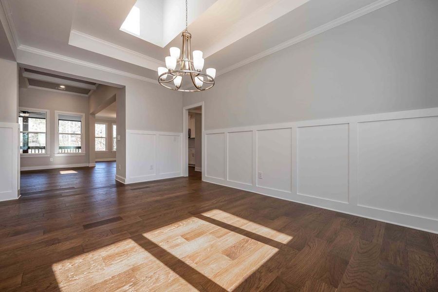 Empty dining room with hardwood floors, white walls with wainscoting, and a chandelier.