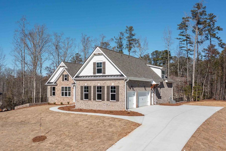 A brick and siding house with a driveway, surrounded by trees and a blue sky.