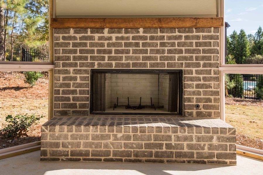 Brick outdoor fireplace on a patio with surrounding glass windows and wood beam above.