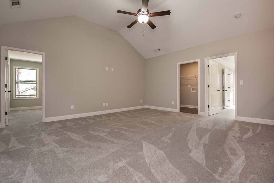 Spacious bedroom with gray carpet, vaulted ceiling, two doorways, and a ceiling fan.