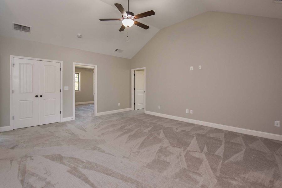 Spacious bedroom with neutral gray walls, carpet, two white doors, and a ceiling fan.