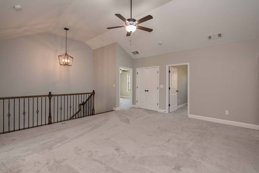 Spacious room with carpet, railing, ceiling fan, light fixture, and doorways.