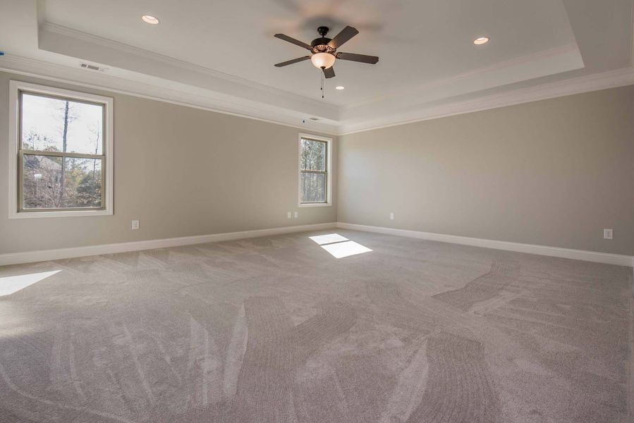 Empty bedroom with gray carpet, light walls, two windows, and a ceiling fan.
