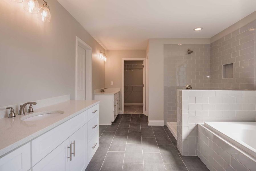 Spacious, modern bathroom with white cabinets, gray tile, glass shower, and a bathtub.