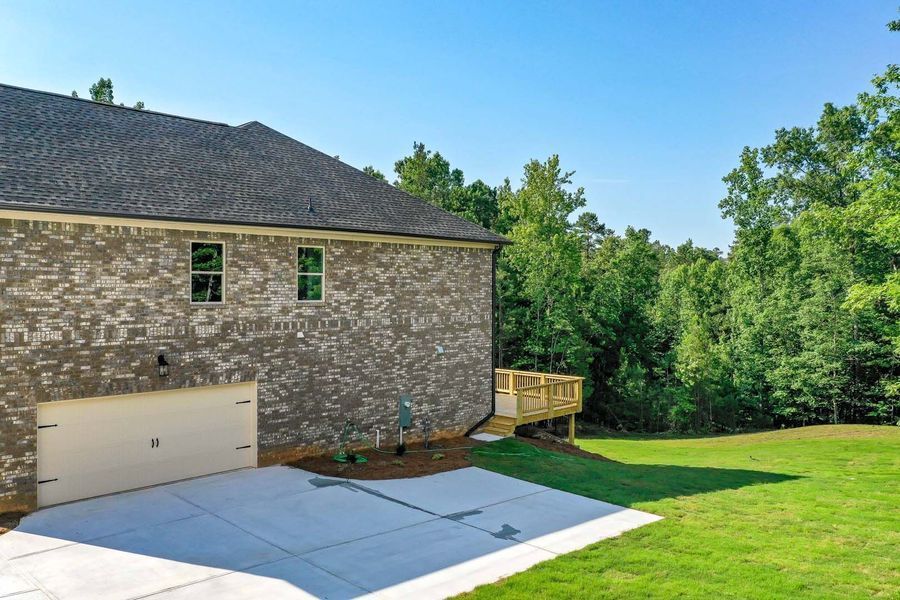 Brick house with garage and small wooden deck, surrounded by green grass and trees.
