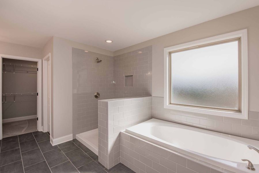 Modern bathroom with a shower, bathtub, frosted window, and walk-in closet with dark tile floor and gray walls.