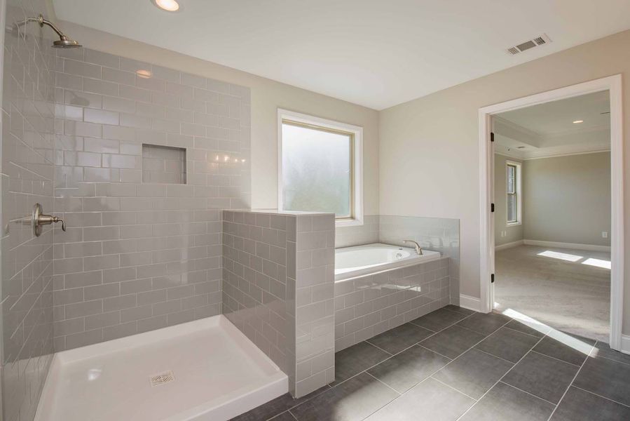 Modern bathroom with grey tile shower and flooring, a built-in tub, and a doorway to a bedroom.