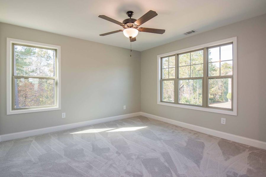 Empty bedroom with gray walls, carpet, and two windows. Ceiling fan.