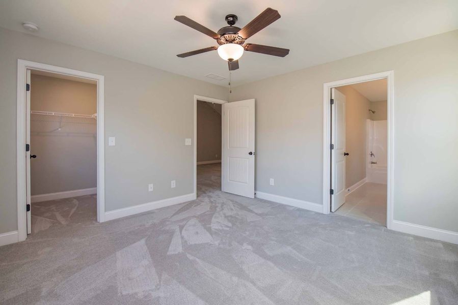 Bedroom with light gray walls, carpet, and three white doors. A ceiling fan hangs from the ceiling.