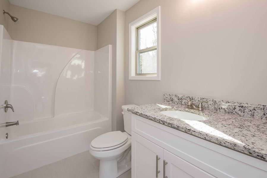 Bathroom with white tub, toilet, and vanity with granite countertop, light gray walls.