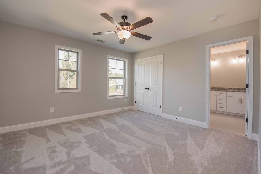 Bedroom with gray walls, patterned carpet, two windows, white door, and open door to a bathroom.