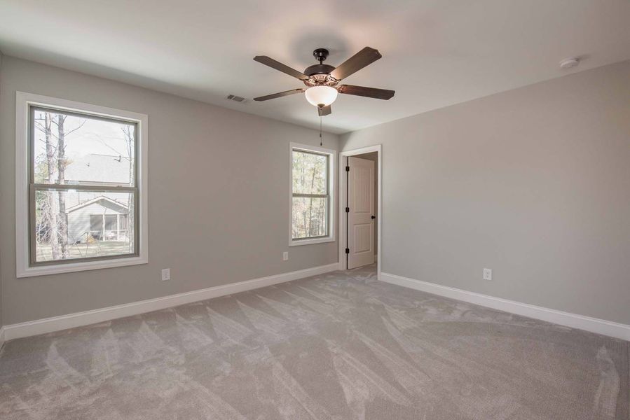 Empty bedroom with gray walls and carpet, two windows, and a ceiling fan.