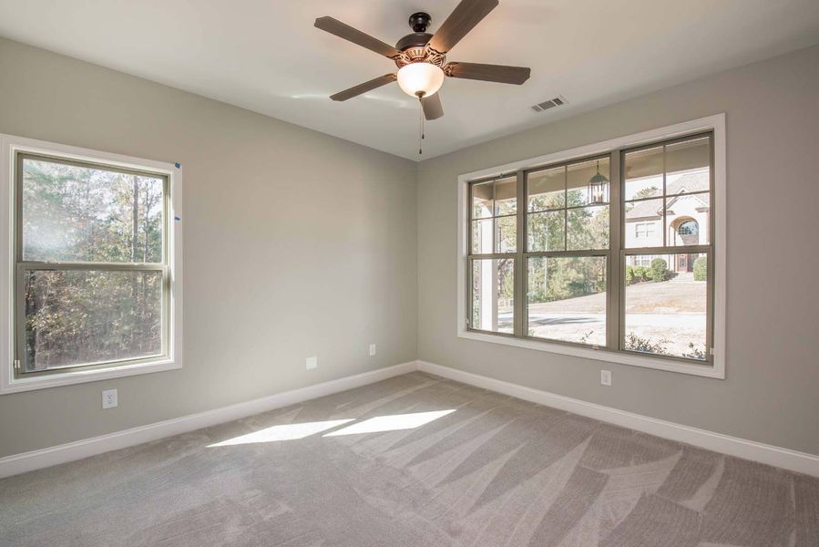 Empty bedroom with gray walls and carpet, two windows, and a ceiling fan.