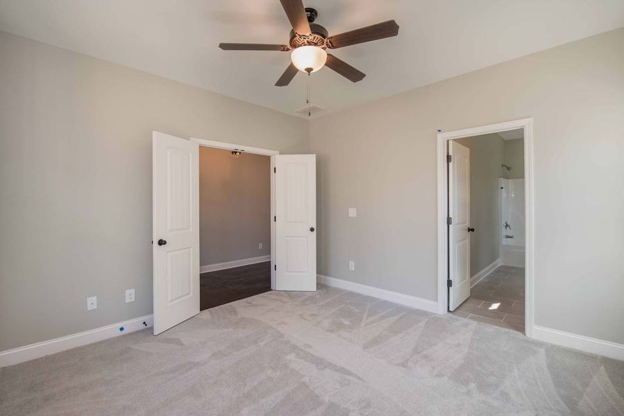 Empty bedroom with gray walls, carpet, and doors to another room and bathroom.