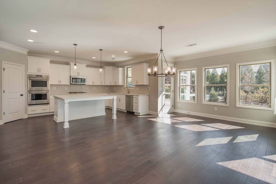 Open-concept kitchen with white cabinets, dark hardwood floors, and large windows.