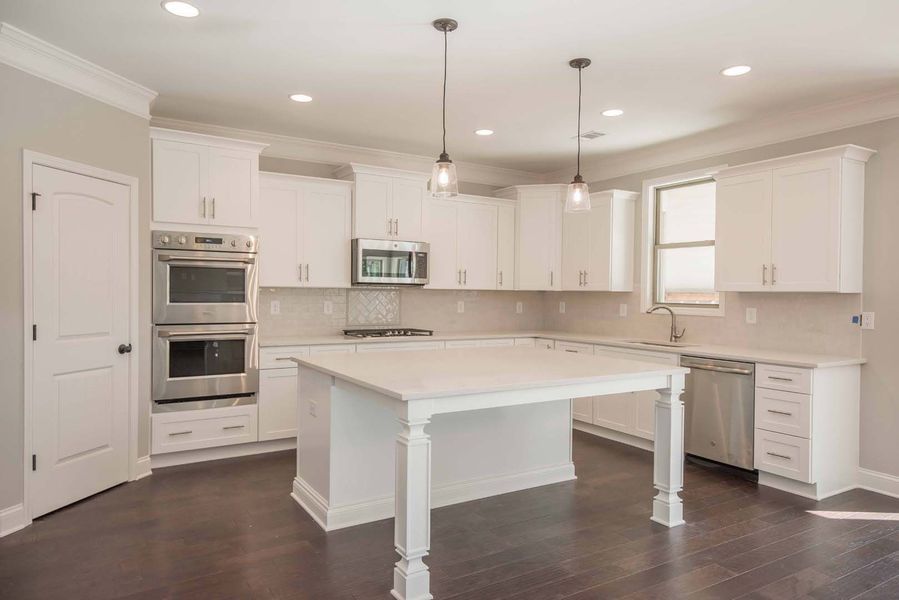 White kitchen with island, stainless steel appliances, dark wood floors, and pendant lights.
