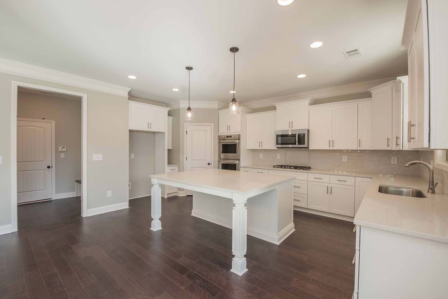 Spacious white kitchen with island, cabinets, dark wood floors, and light fixtures.