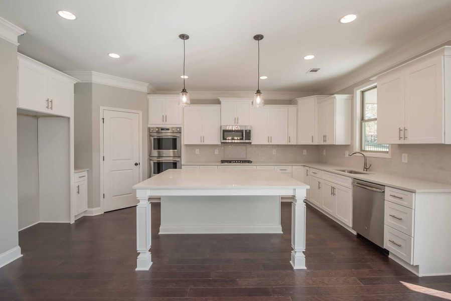 Modern white kitchen with island, dark wood floors, and pendant lights.