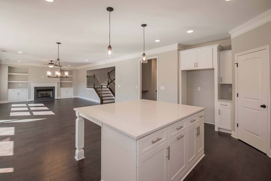 Spacious, bright kitchen with white island, dark hardwood floors, and open to living area with fireplace.