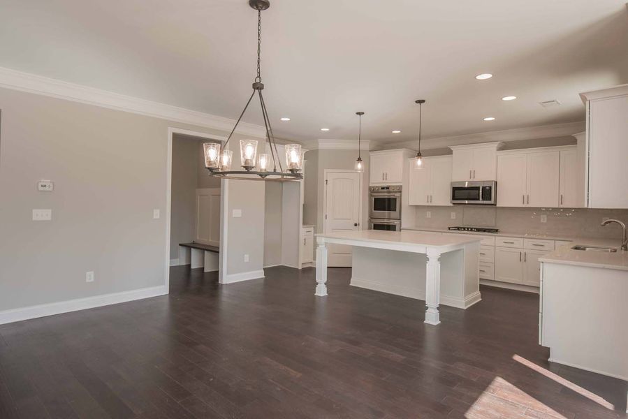 Open-concept kitchen with white cabinets, dark wood floors, and a large island. A chandelier hangs overhead.