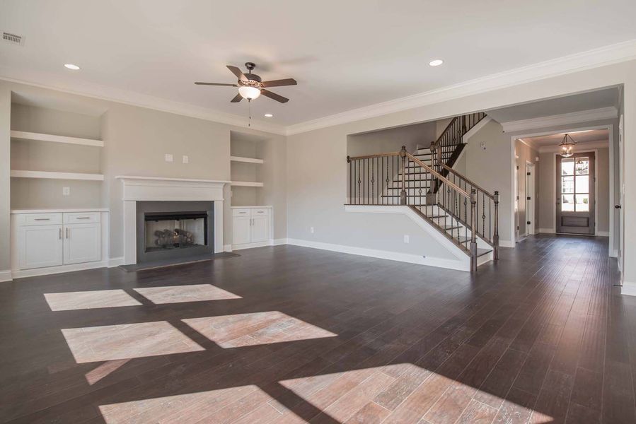 Spacious living room with dark hardwood floors, fireplace, staircase, and built-in shelving; neutral walls.
