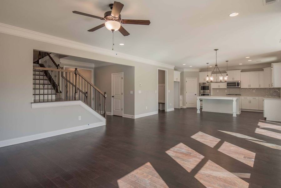 Open-concept living space with stairs, kitchen, and dark wood floors. White walls and cabinetry.