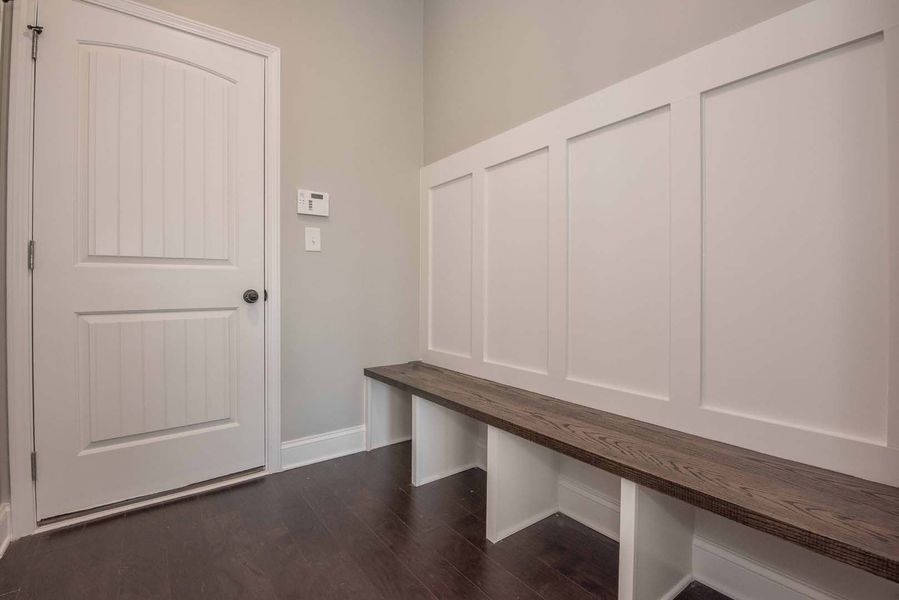 Mudroom with white paneling, bench, and dark wood floor.